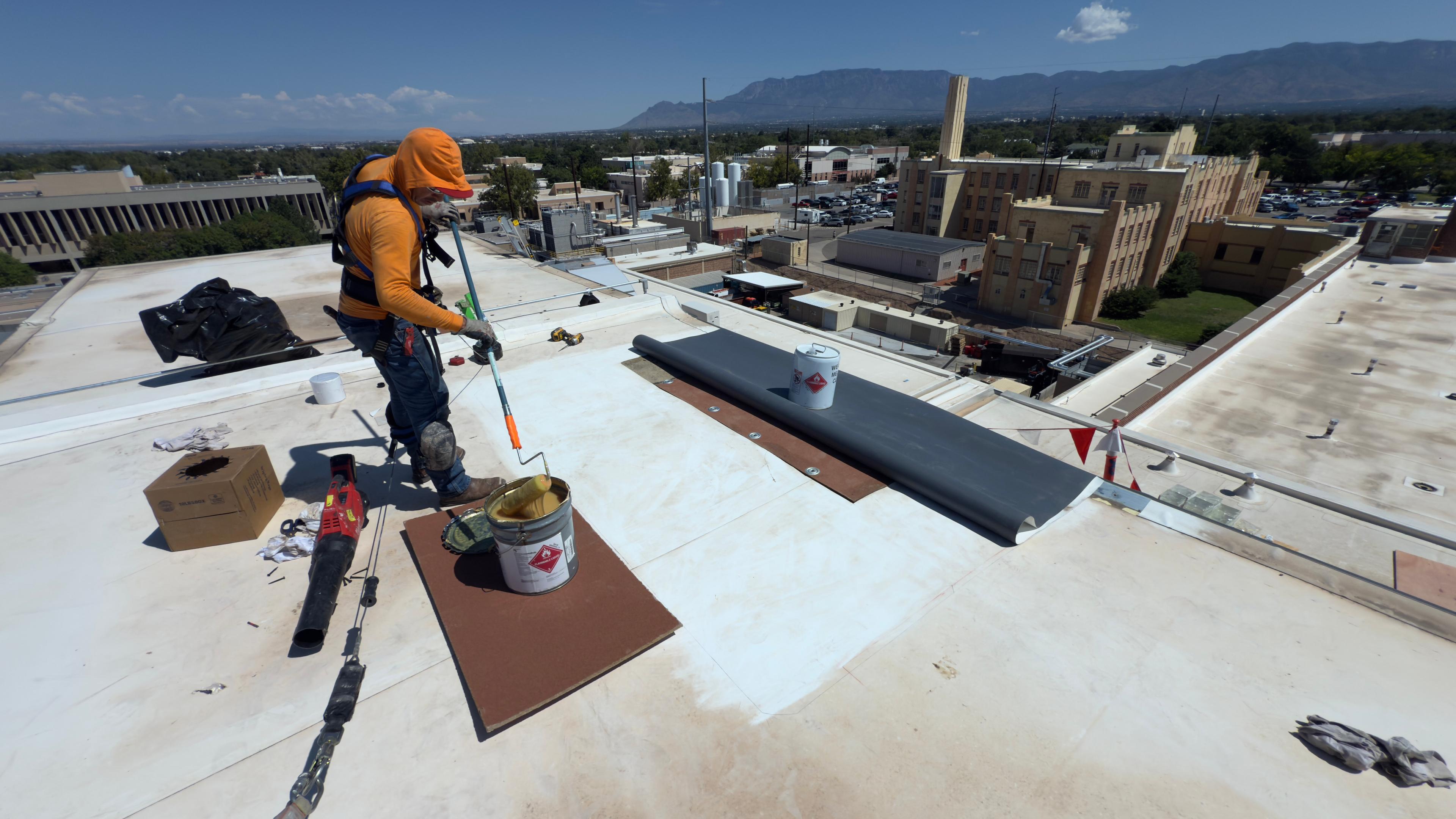 Wide commercial roofing jobsite with crew member working on a large roof